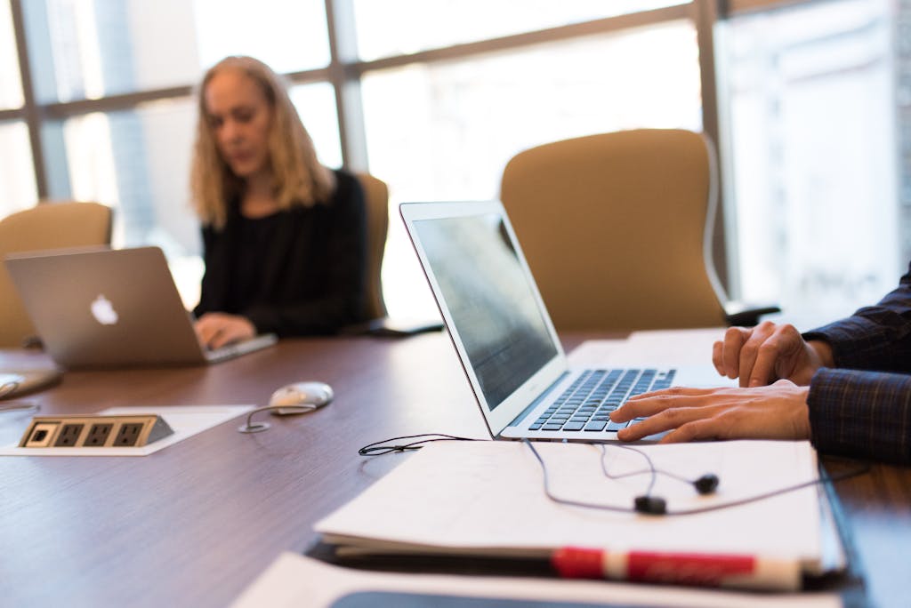 Colleagues collaborating in a bright, modern office setting, focused on laptop work.